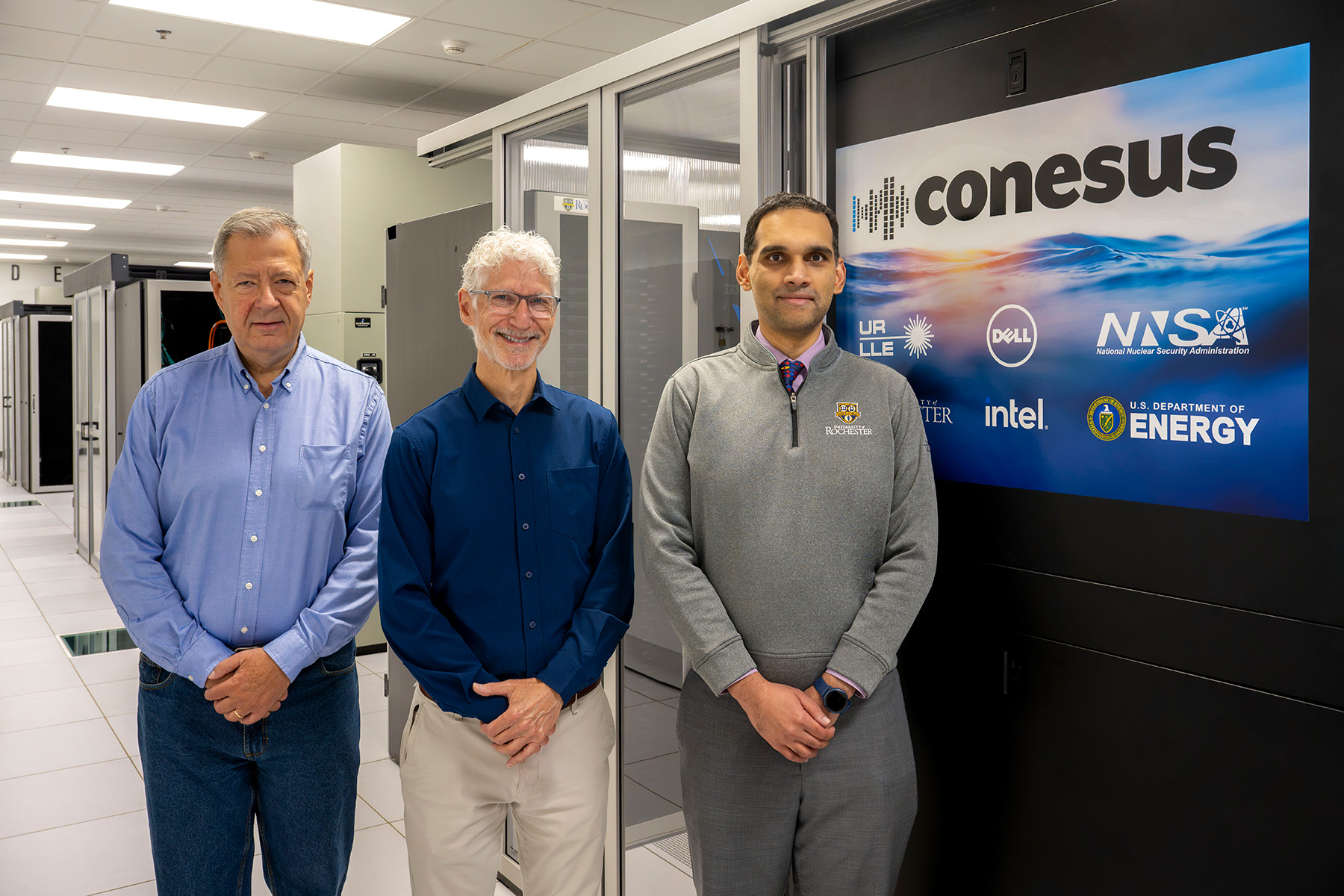 Group photo of Riccardo Betti, Mark Guardalben, and Varchas Gopalaswamy standing in front of Conesus computer cluster at the University of Rochester’s Primary Data Center.