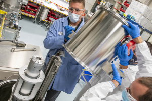 Three technicians putting the spool on the Moving Cryogenic Transfer Cart (MCTC).